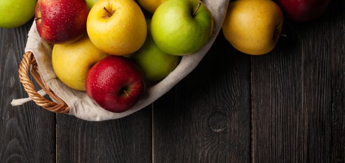 Fruits de pomme mûrs colorés dans un panier sur une table en bois.