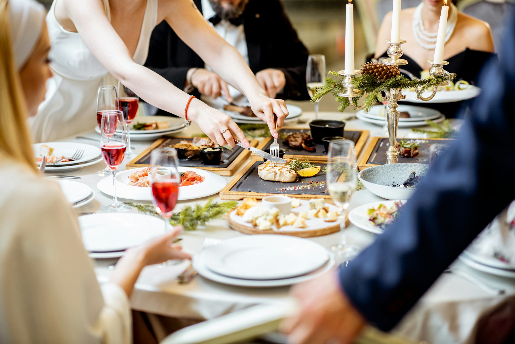 Personnes ayant un dîner de fête à une table bien servie avec des plats savoureux pendant le réveillon du Nouvel An au restaurant de luxe, vue rapprochée sans visage