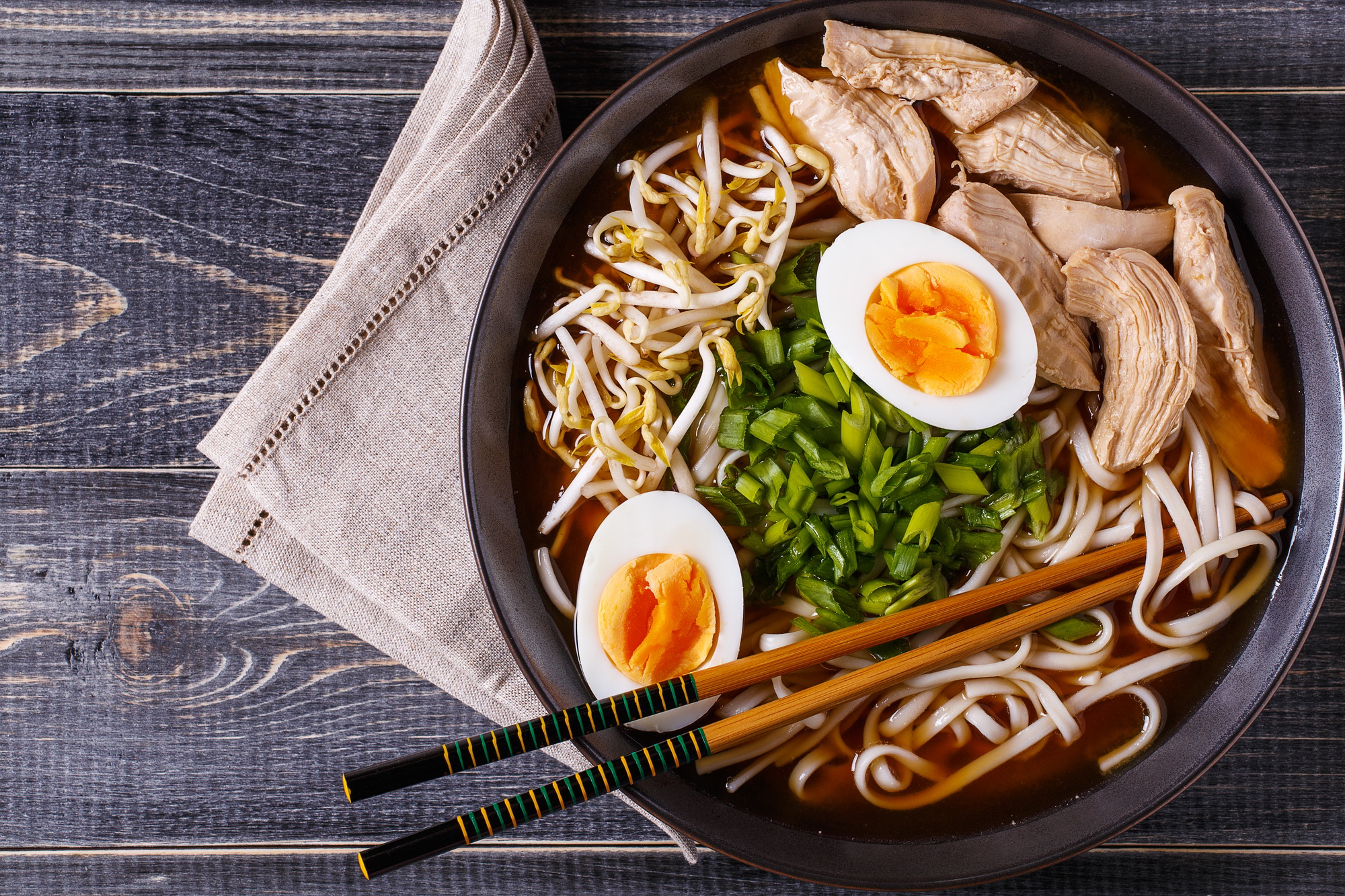 Soupe de ramen japonaise avec poulet, œuf, ciboulette et germe sur fond en bois foncé.