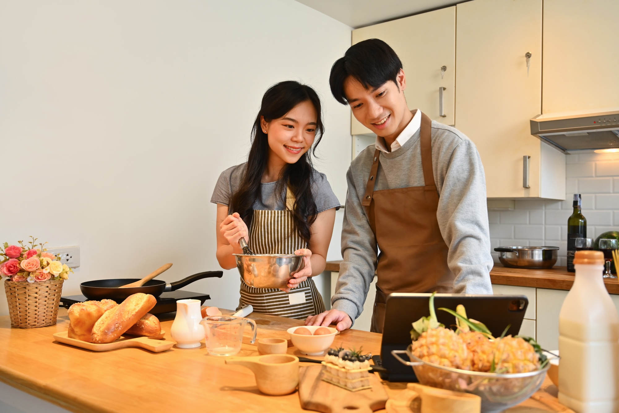 Beau jeune couple cuisine dans la cuisine et suivant une recette en ligne sur la tablette numérique.