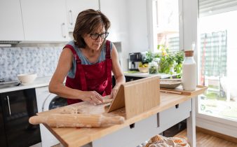 Femme âgée concentrée portant une pâte à pétrissage de tablier tout en s'engageant dans un cours de cuisine en ligne sur sa tablette numérique, en profitant de la créativité culinaire dans sa cuisine confortable