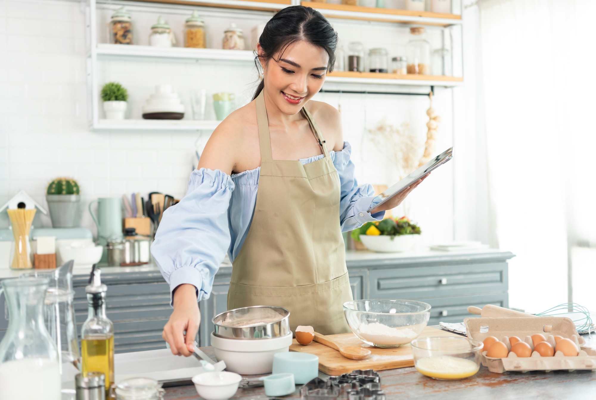 Jeune femme au foyer asiatique dans la cuisine à l'aide de la tablette pour rechercher des recettes en ligne cuisine la boulangerie maison maison.