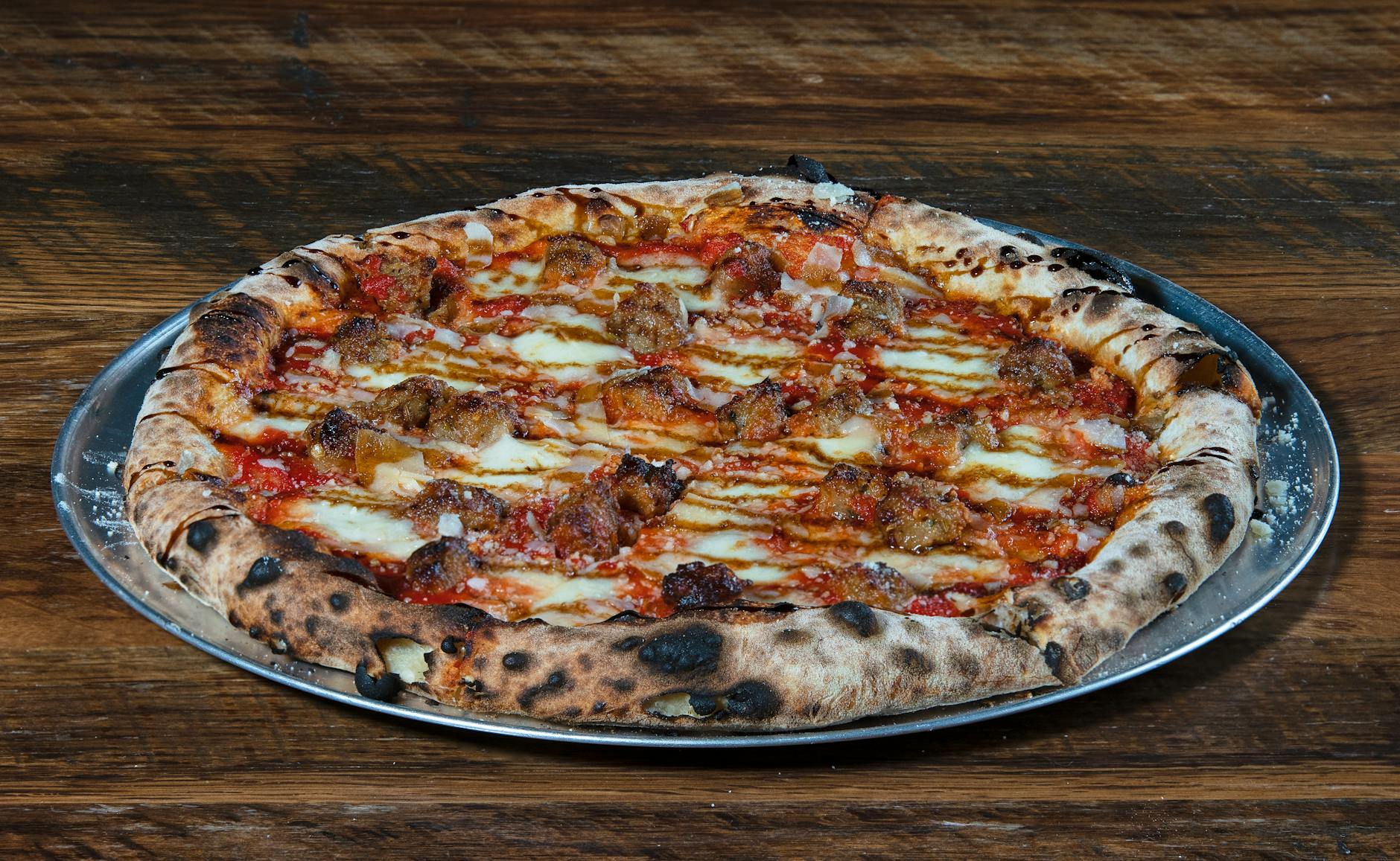 Délicieuse pizza à bois avec saucisse italienne sur un plateau en métal.