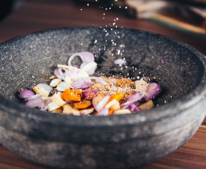 Le gros plan de l'assaisonnement est ajouté aux ingrédients frais dans un bol en pierre, parfait pour les thèmes culinaires.