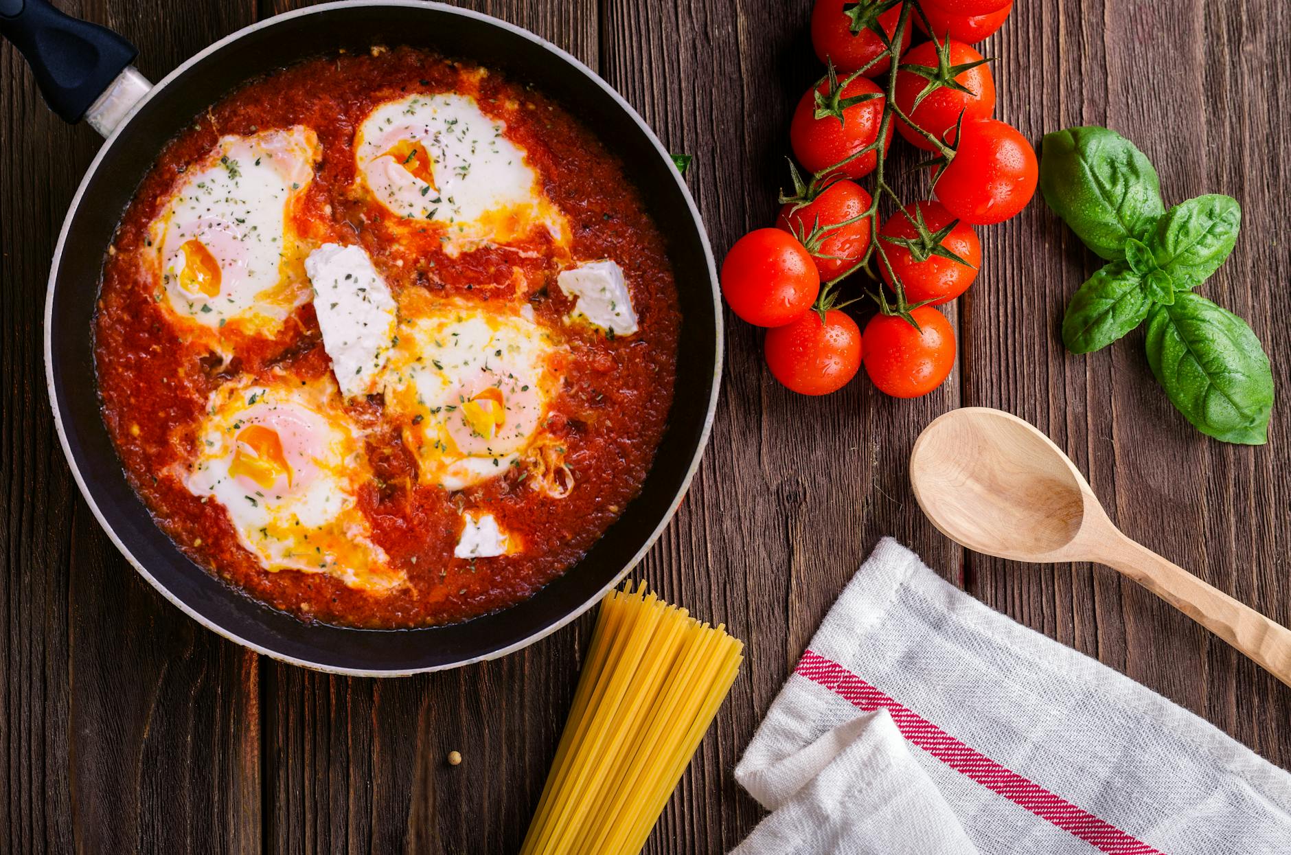 De délicieux œufs en sauce tomate avec du basilic, des spaghettis et des tomates fraîches sur une table en bois.