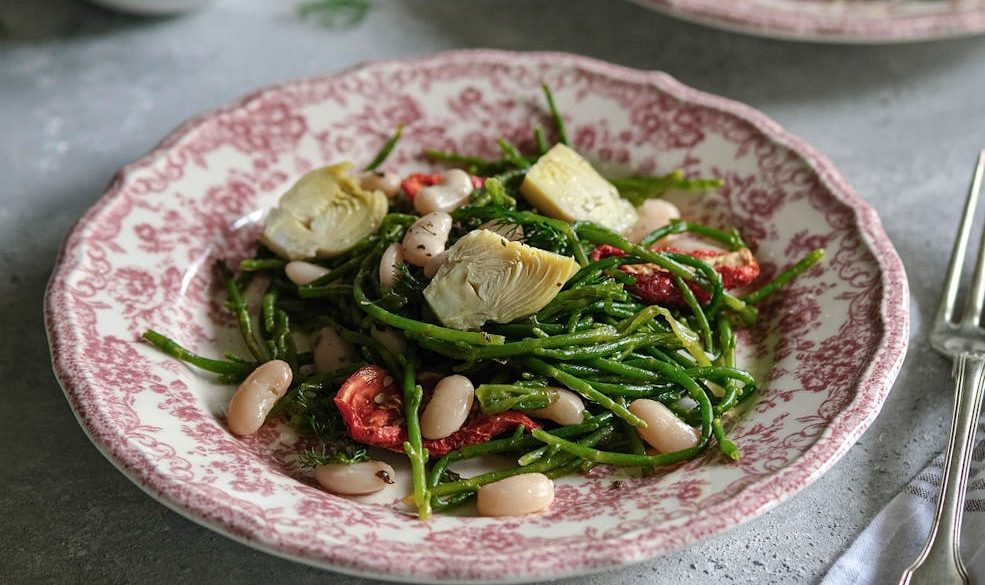 Délicieuse salade végétalienne avec des artichauts, des haricots et des légumes verts, servi sur une assiette décorative.