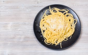 Cuisine italienne - Vue de dessus des spaghetti al Burro e Parmigiano (pâtes au beurre et fromage) sur une assiette noire sur fond en bois gris avec copyspace vierge