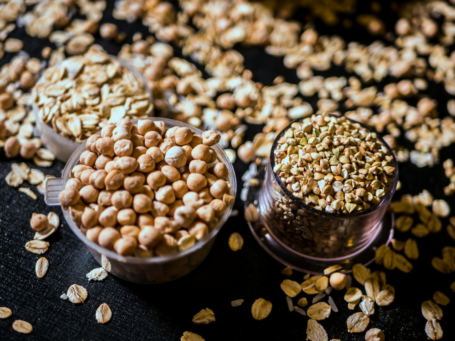 Gros plan de grains bruts et de graines assortis en tasses sur fond sombre, présentant la variété et la texture.