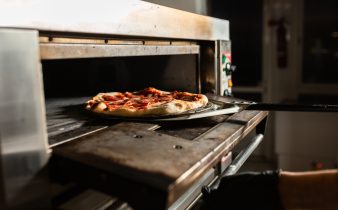 Pizza au pepperoni fraîchement préparée, sortant du four d'une pizzeria avec une pelle en métal.