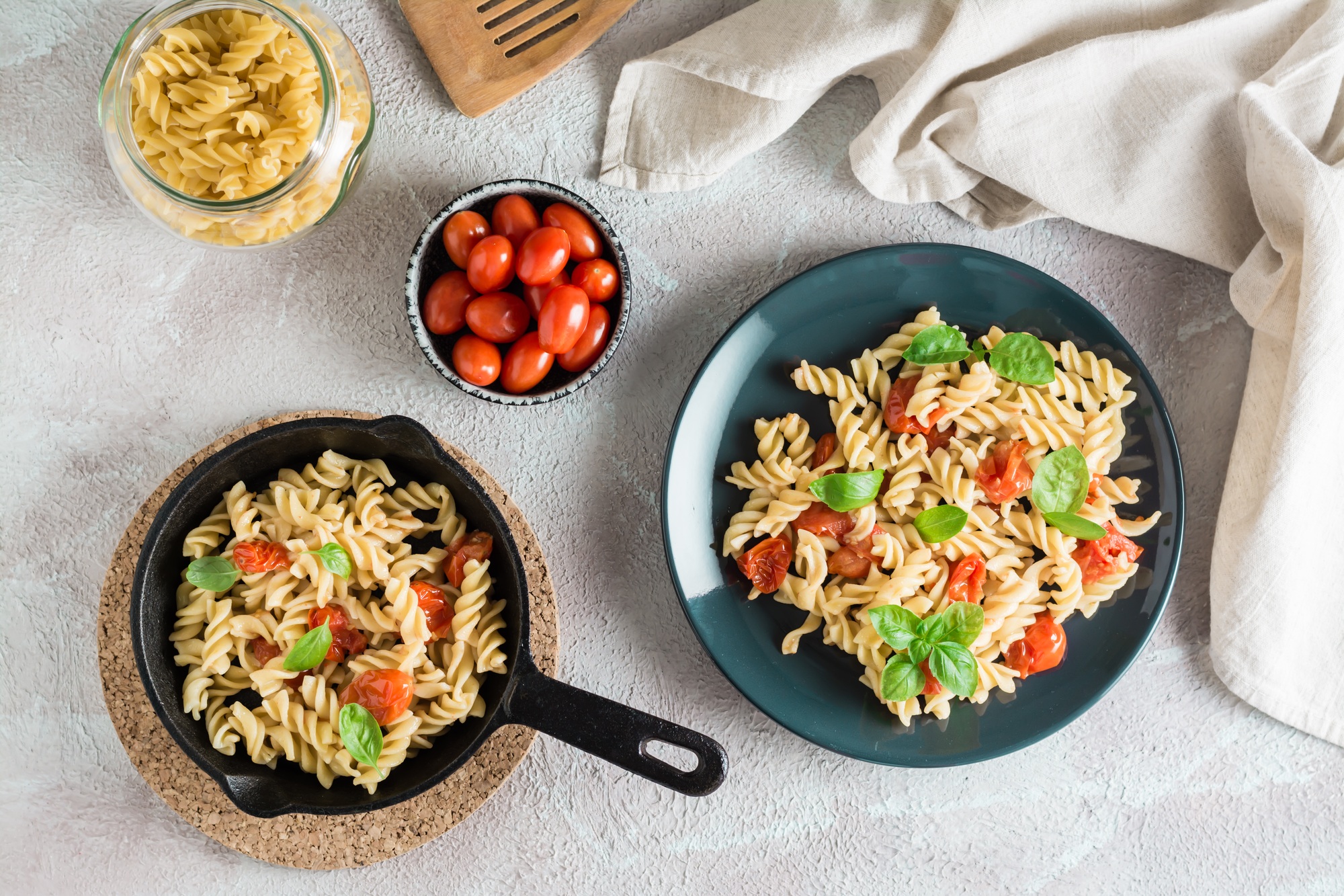 Une assiette de pâtes avec des tomates et du basilic sur une assiette et des ingrédients de cuisson sur la table.