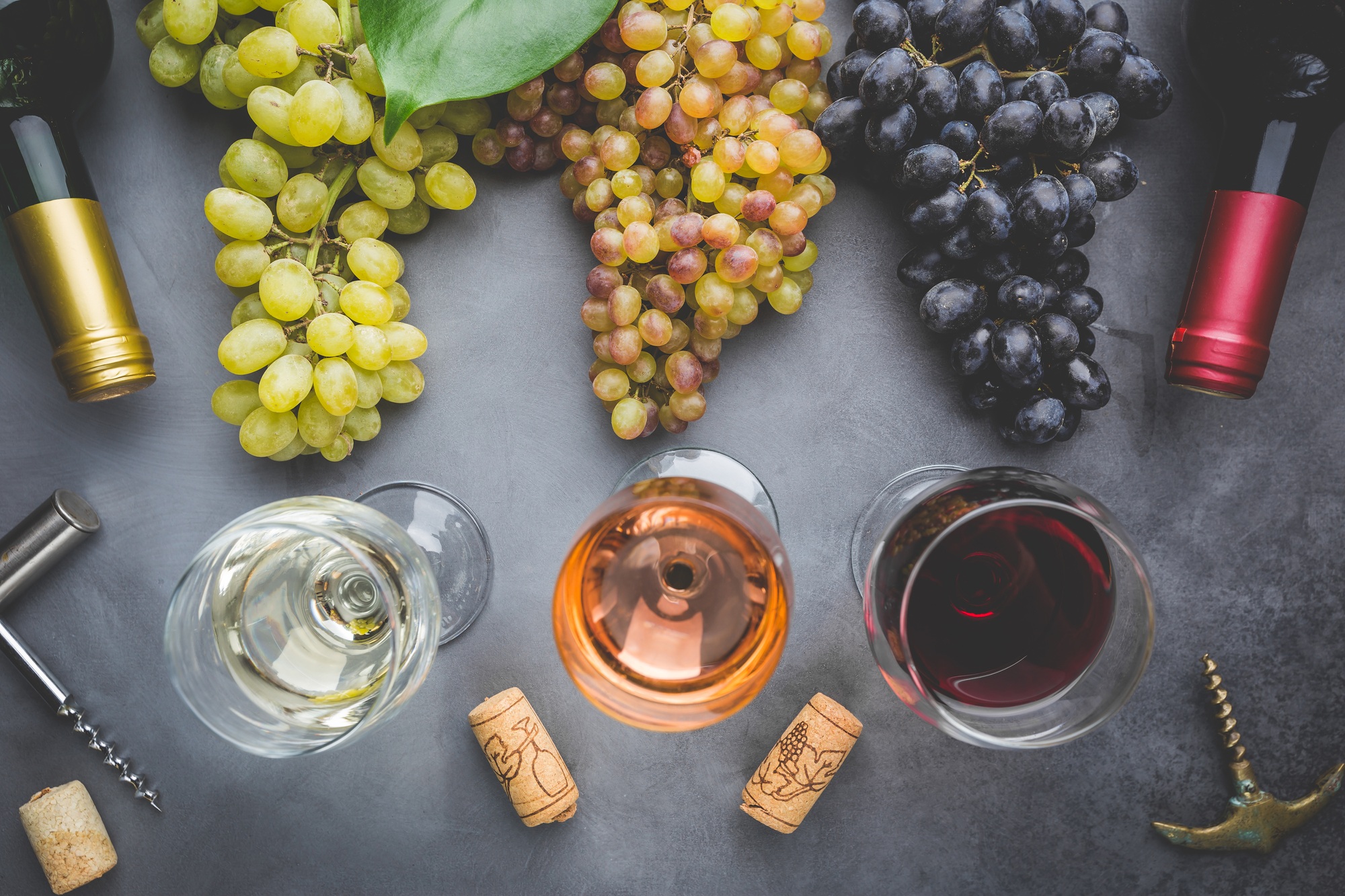 Lunettes avec vin blanc, rouge et rose et raisins mûrs sur fond en pierre noire, vue sur le dessus