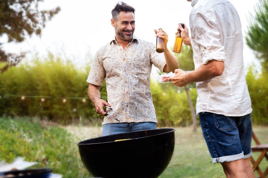 Deux amis masculins grillant avec de la bière tout en cuisinant de la nourriture sur le gril.