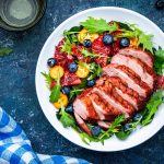 Salade de canard avec poitrine grillée avec orange rouge, kumquat, myrtille et bette à carde, frisse, mizuna et feuilles de roquette sur fond de table bleue, vue sur la vue