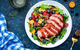 Salade de canard avec poitrine grillée avec orange rouge, kumquat, myrtille et bette à carde, frisse, mizuna et feuilles de roquette sur fond de table bleue, vue sur la vue