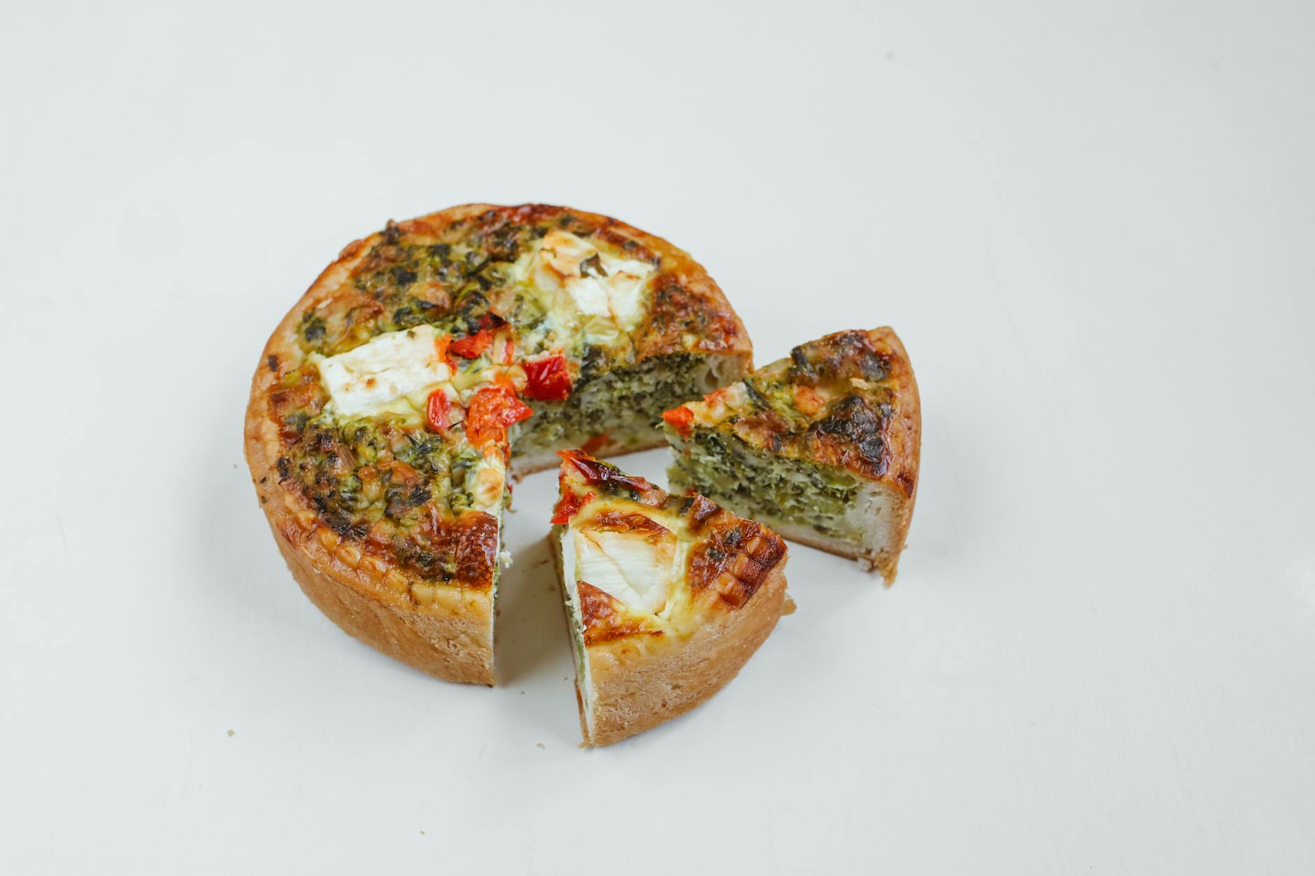 Délicieuse quiche aux épinards et au fromage avec des tomates cerises sur fond blanc, parfaite pour tout repas.