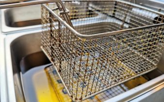 Gros plan d'un panier de friteuses en acier inoxydable sur l'huile de cuisson chaude, mettant l'accent sur l'artisanat métallique.