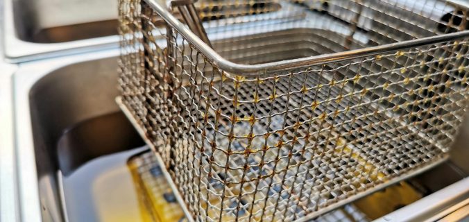 Gros plan d'un panier de friteuses en acier inoxydable sur l'huile de cuisson chaude, mettant l'accent sur l'artisanat métallique.