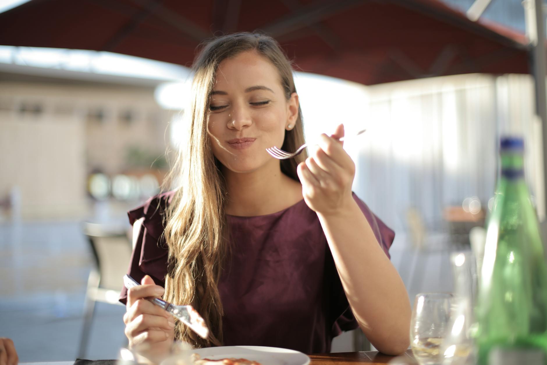 Une femme savourant son repas avec le sourire, dînant en plein air dans un cadre agréable.