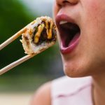Femme mangeant des sushis avec des baguettes à l'extérieur, présentant des photographies culinaires vibrantes.