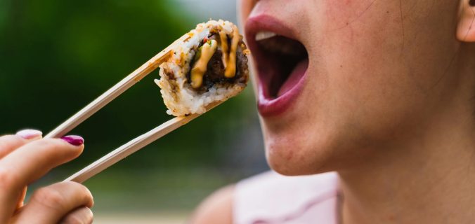 Femme mangeant des sushis avec des baguettes à l'extérieur, présentant des photographies culinaires vibrantes.