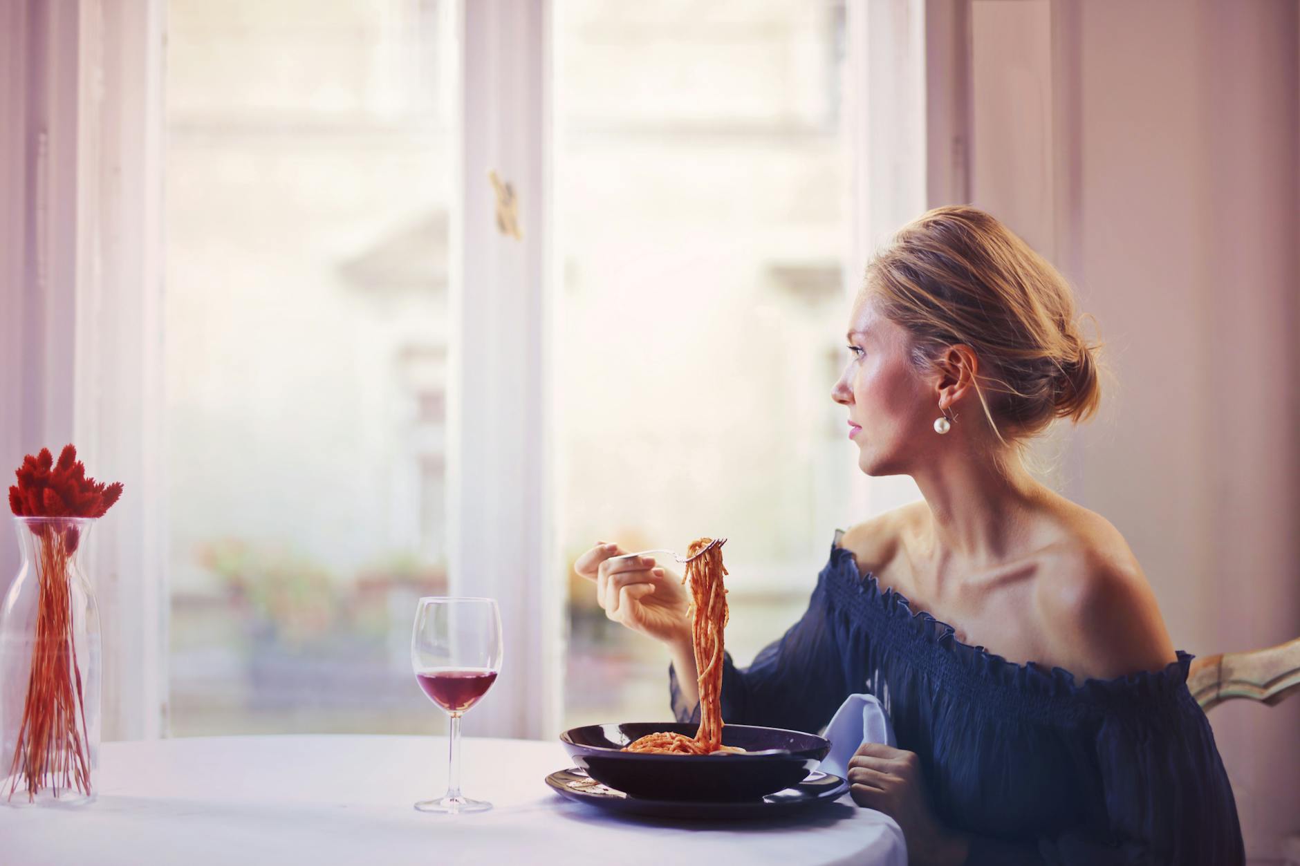 Une femme savourant un repas de spaghetti et de vin à une table de restaurant, élégamment habillée.