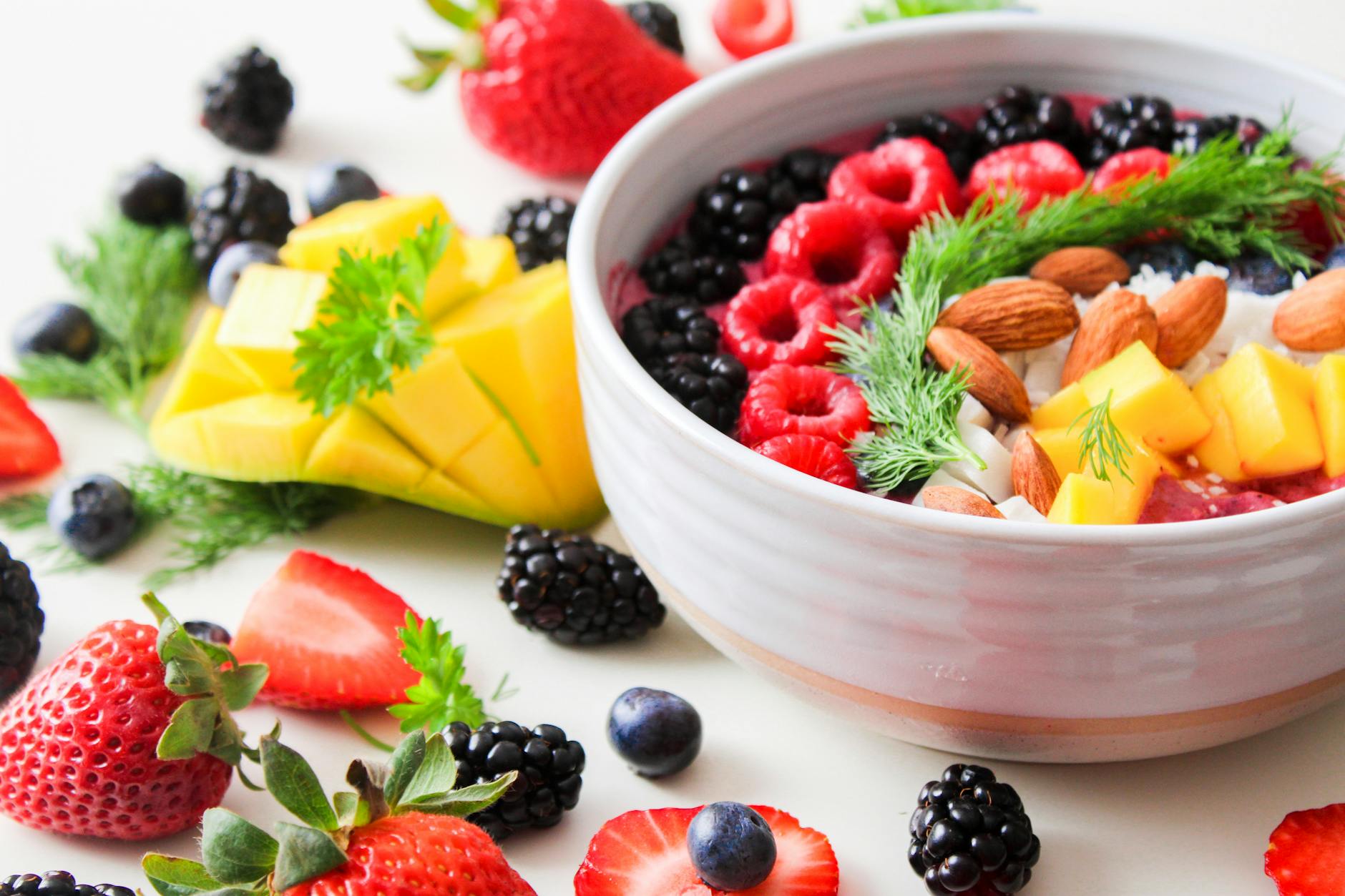 Un bol vibrant rempli de baies fraîches, de mangue, d'amandes et d'herbes, parfait pour une collation ou un petit-déjeuner sain.